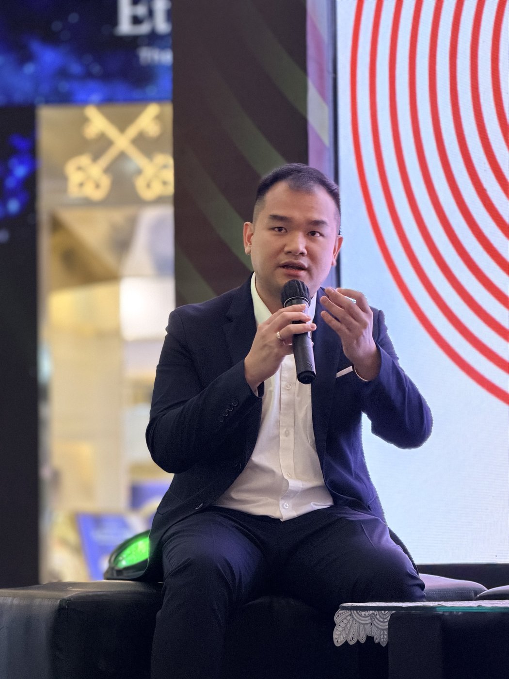 Anthony Kusumoputro speaking into a microphone on stage, gesturing with his free hand.