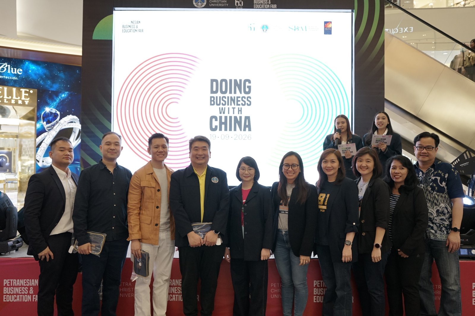 A large group of speakers, staff and student organisers standing together in front of the event screen after the talk.